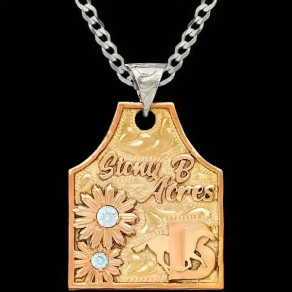 A golden bronze cow tag necklace featuring personalized copper lettering, ranch brand and flowers