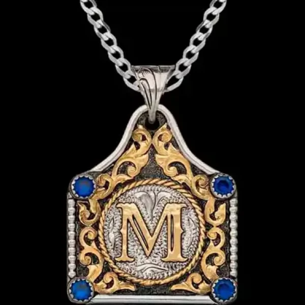 A cow tag necklace featuring a golden initial, bronze scrollwork and blue zirconia stones 