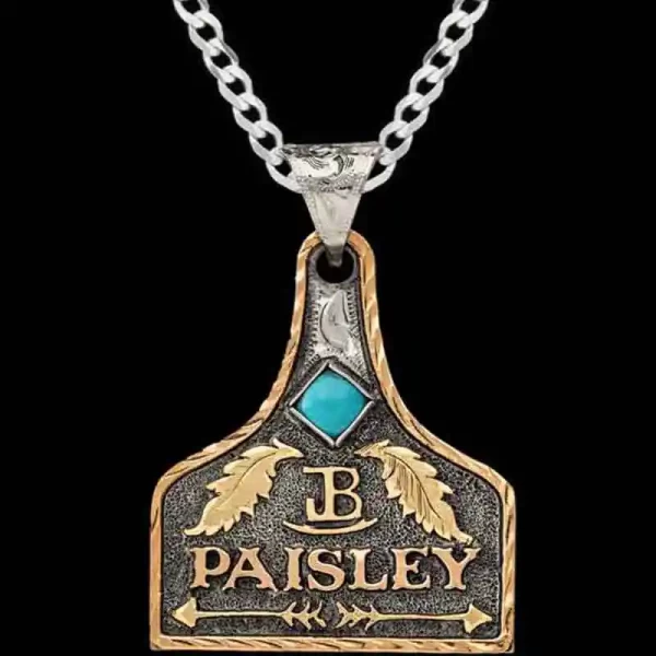 A matted silver cow tag necklace featuring bronze custom lettering, ranch brand, arrows, feathers and turquoise stone