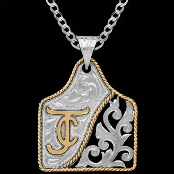 A cow tag necklace featuring a bronze ranch brand and silver scrollwork with black enamel background