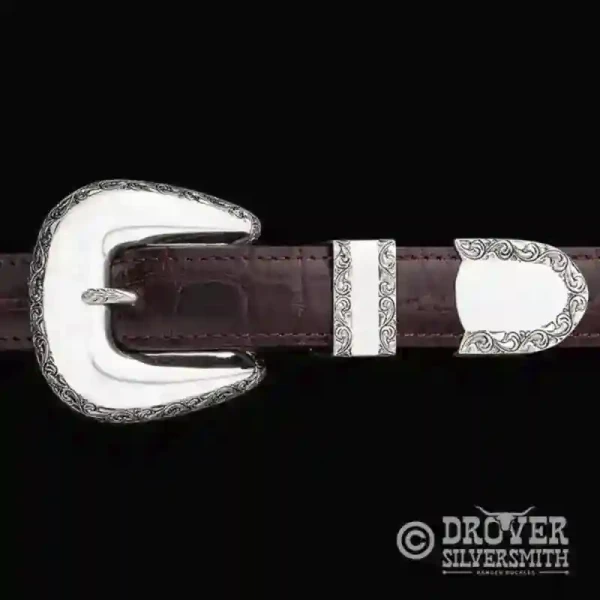 A sterling silver belt buckle set featuring 3d scrollwork with golden bronze hand engraced accents. 