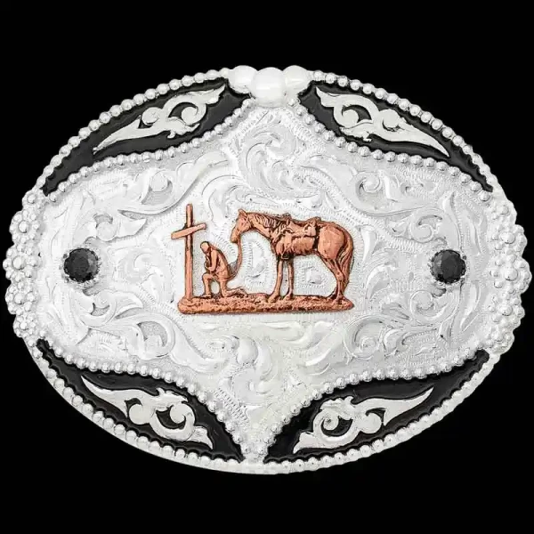 A custom oval western belt buckle featuring a praying cowboy to a cross figure