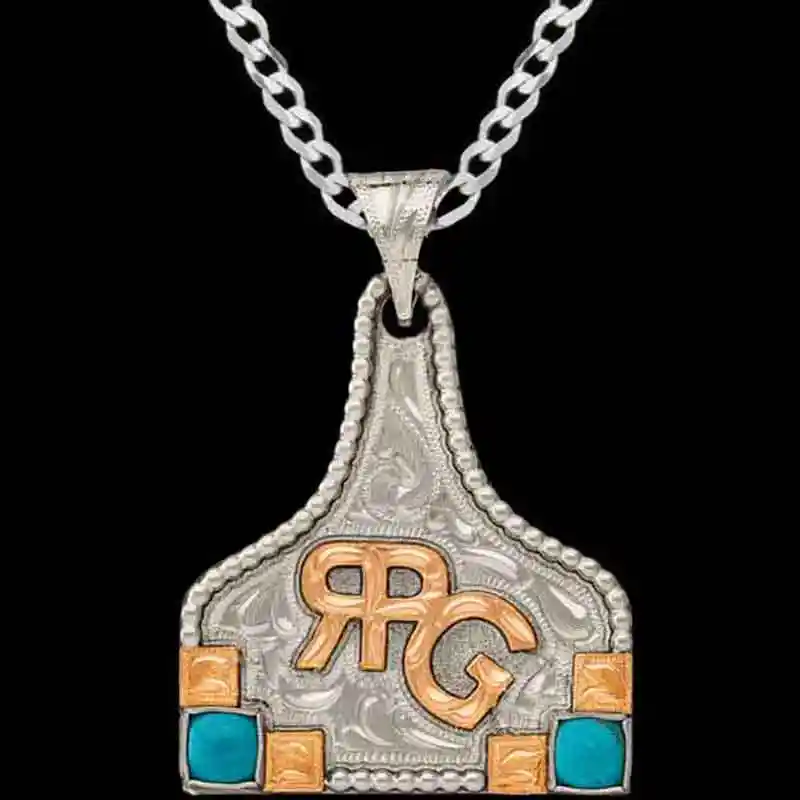A hand engraved silver cow tag necklace featuring a copper custom ranch brand and turquoise stones 
